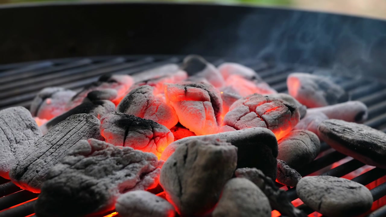Glowing Charcoal Briquettes On Grill, Closeup Of Red Embers And Thin Smoke Rising From Steel Grate, Backyard