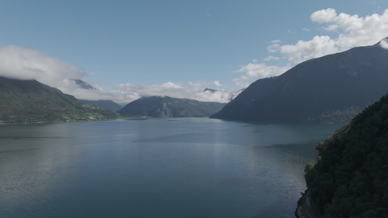 노르웨이의 피오르드를 향해 물 위로 오는 느린 속도 드론 은 고 구름이 많은 날, 배경에는 산과 초록색과 반사되는 물 로그가 있습니다.
