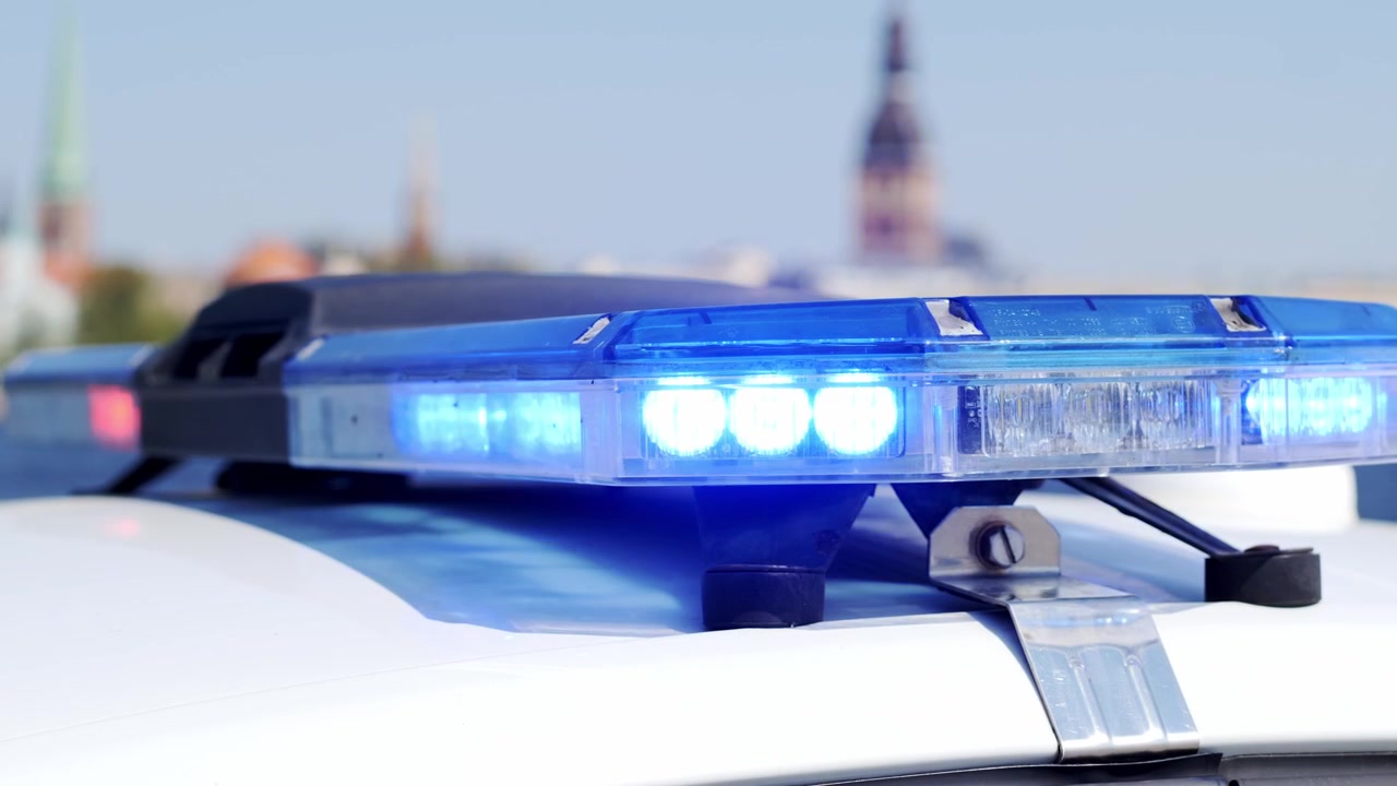 Luci blu della polizia lampeggiano in primo piano mentre lo skyline di Riga sfuma dolcemente sullo sfondo
