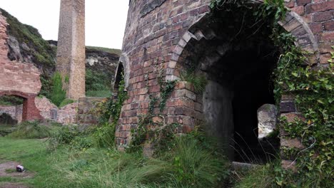 Panning-across-grassy-Porth-Wen-abandoned-brickwork-furnace-ruins,-Anglesey-industrial-site