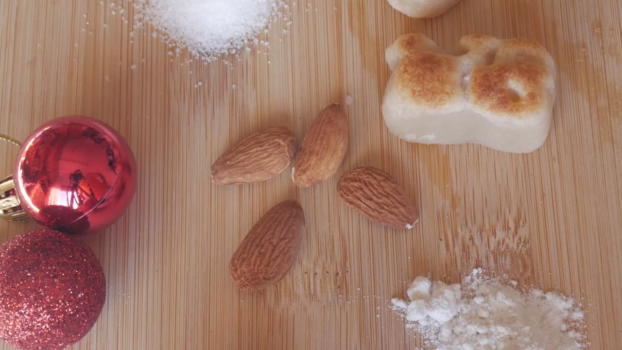 Top-down shot of toasted marzipan pieces, almonds, and sugar on a wooden surface decorated with red Christmas ornaments