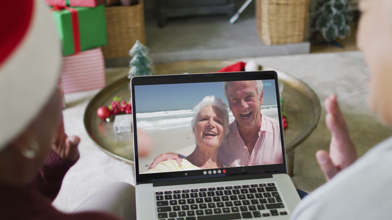 diversas amigas mayores que usan una computadora portátil para una videollamada de navidad con una pareja feliz en la pantalla