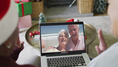 Diverse-senior-female-friends-using-laptop-for-christmas-video-call-with-happy-couple-on-screen