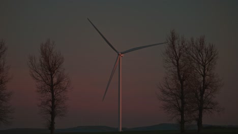 Wind-turbine-spinning-between-leafless-trees-at-dusk-in-slow-motion