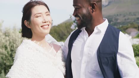 Video-portrait-of-happy-diverse-bride-and-groom-smiling-to-camera-at-outdoor-wedding