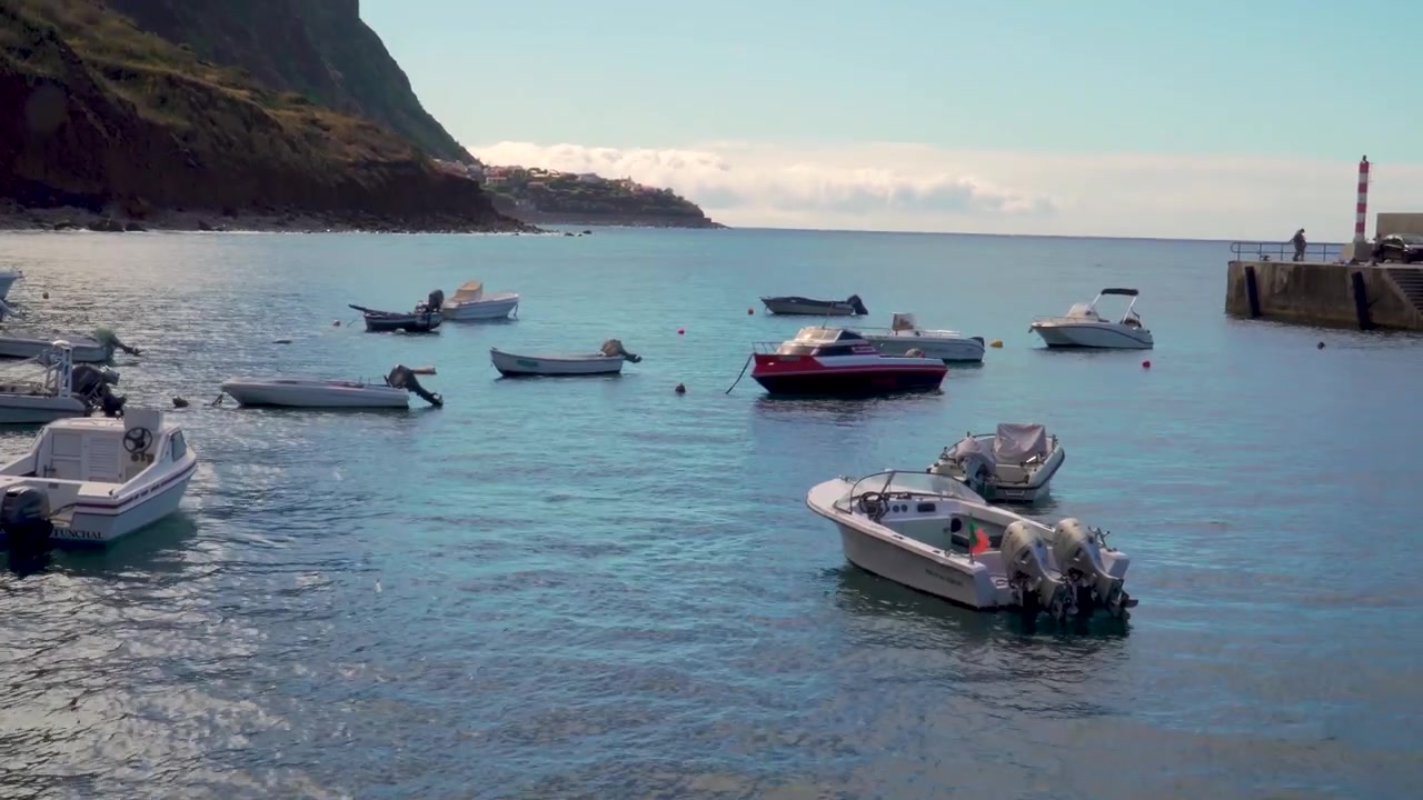 Ripresa cinematografica panoramica di Paul do Mar con le tradizionali canoe dei pescatori che galleggiano dolcemente accanto al molo. Le calme acque dell'Atlantico riflettono gli scafi colorati delle imbarcazioni