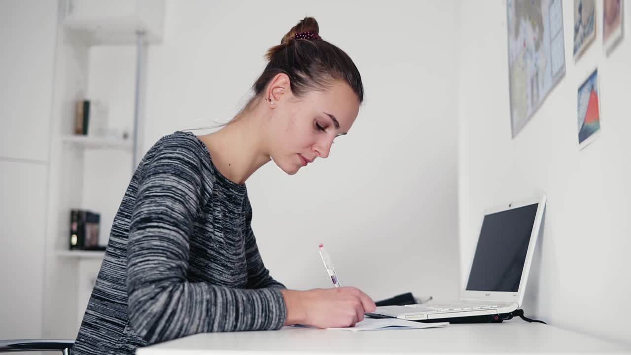 hermosa joven sentada junto a la mesa y escribiendo una carta usando su bolígrafo. abrir la computadora portátil en la mesa. mujer de negocios haciendo