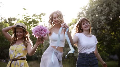 Women-friendship.-Three-attractive-girls-in-summer-outfits.-Holding-hands-together,-walking-playfully-in-the-forest.-Happy,-smiling