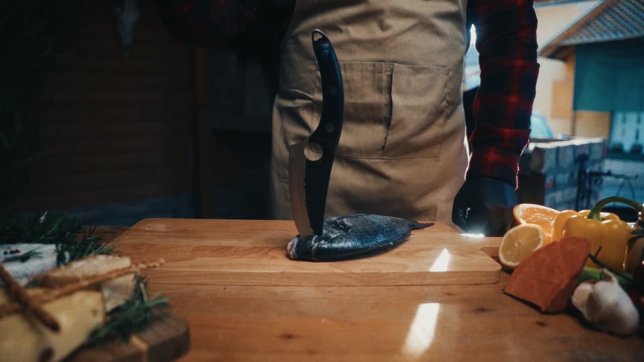 요리사는 나무 테이블 위에 재료와 도구로 밖에서 신선한 물고기를 필레합니다.