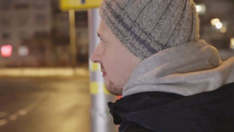 Man-with-winter-hat-standing-near-street-at-night-city,-orbit-view