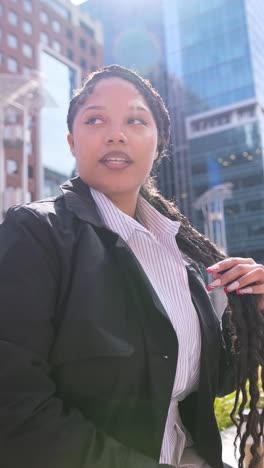 an african american woman stands confidently in a vibrant city environment, beautifully illuminated by warm sunlight. vertical video