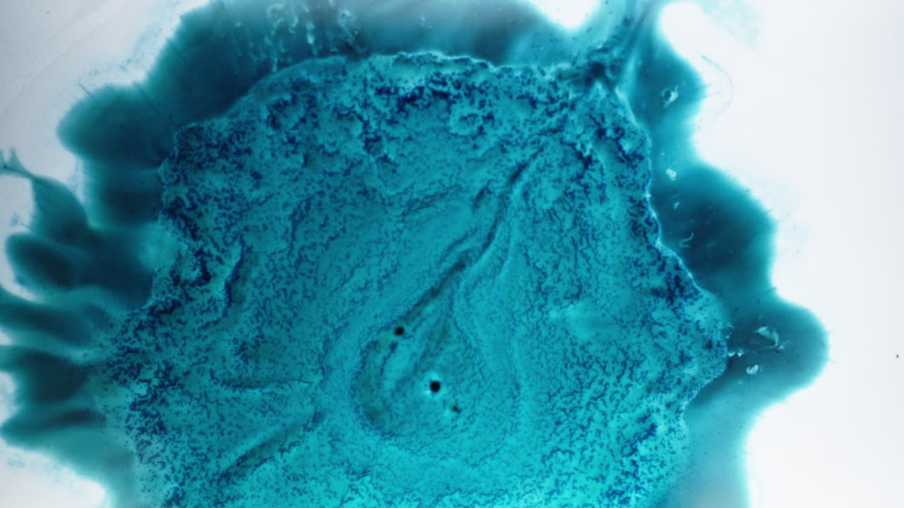 Bright blue ink swirling and spreading in water, close-up macro shot showing fluid movement
