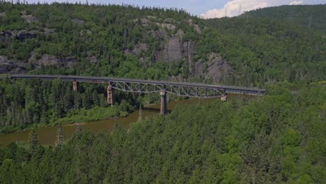 Aerial-drone-footage-of-a-railway-winding-through-a-dense-forest,-featuring-a-scenic-bridge