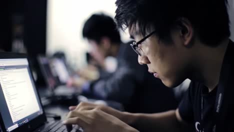 focused student engaging in coding and problem solving during a tech workshop or competitive programming event with multiple laptops in the background