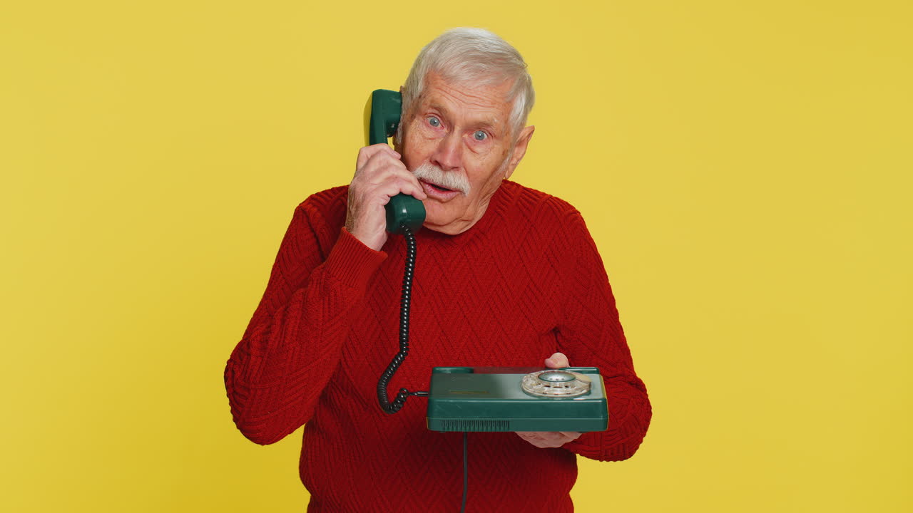 Senior man talking on wired landline vintage telephone advertising proposition of conversation
