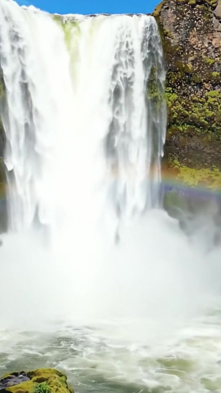 Maestosa Cascata Circondata da Vegetazione Lussureggiante e Nebbia, che Mostra la Bellezza Dinamica della Natura con un Arcobaleno Mozzafiato che si Inarca Sull'Acqua che Scorre