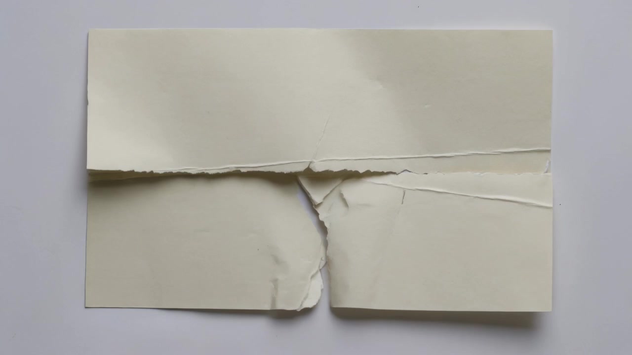 Tearing cream paper from short top tear, splitting downward on white table, showing jagged edges