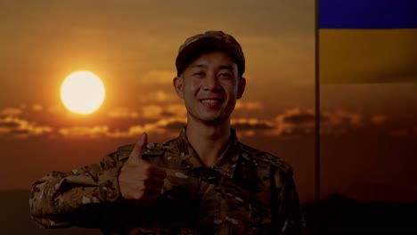 soldado sonriente en uniforme de camuflaje con los pulgares hacia arriba contra la bandera ucraniana al atardecer