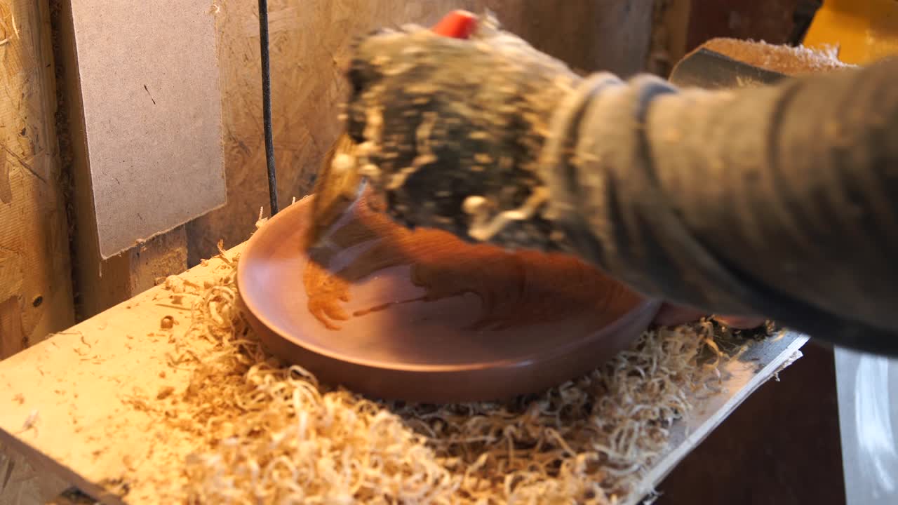 Carpenter oiling wooden dish at workspace.