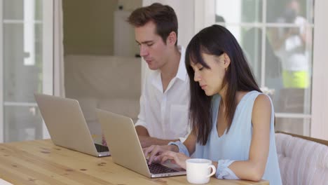 una pareja joven y tranquila sentada en la mesa usando una laptop