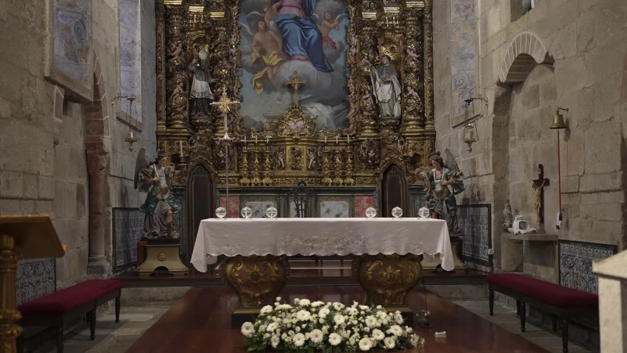 Church altar with a white cloth, ornate golden decorations, and religious statues in the background