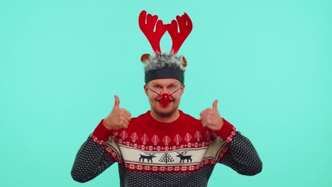 funny man wears red new year sweater deer antlers raises thumbs up agrees with something good, like