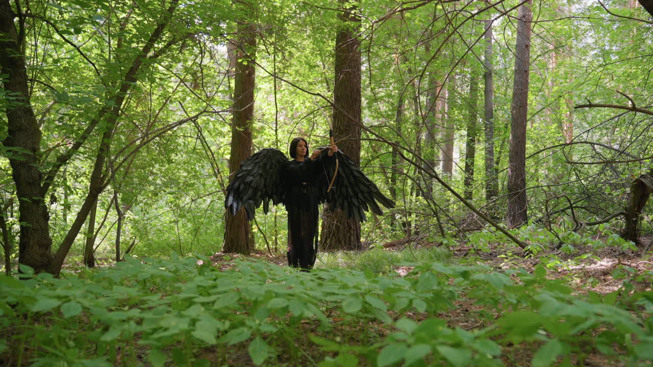 Black fairy with large wings stands in green forest aiming arrow, surrounded by sunlight filtering through trees, creating atmosphere of focus, power, and mystic energy