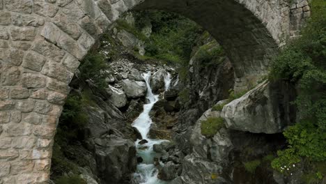 flying under arch of brick bridge while river water stream is flowing in summer season in furka pass valley of switzerland