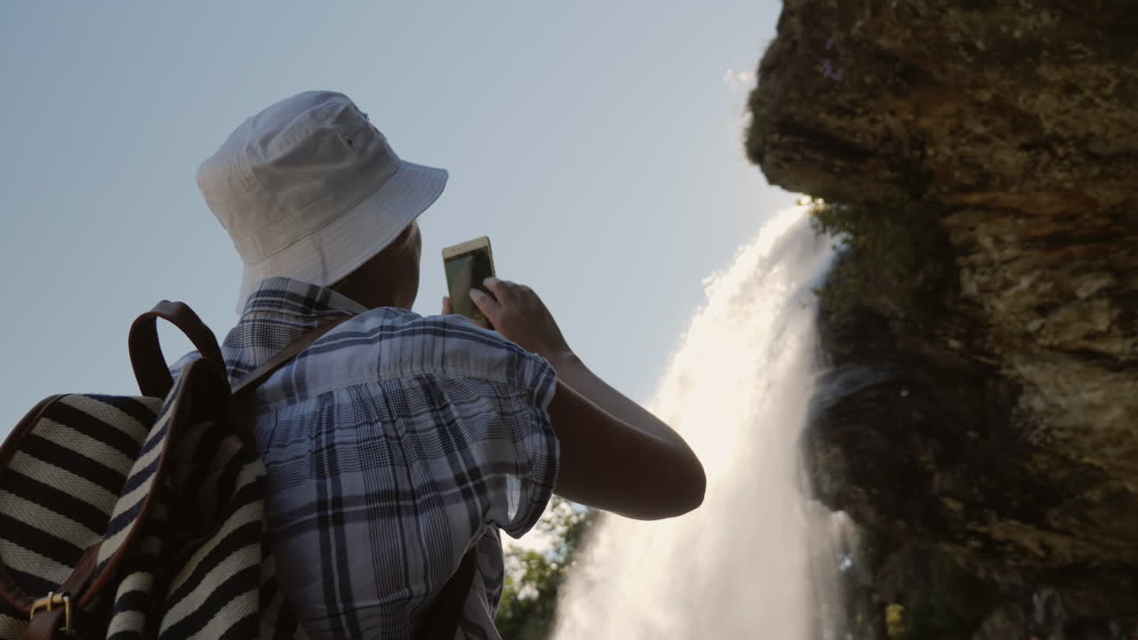 una mujer parada debajo de una cascada steinsdalsfossen toma una foto encima de ella cuelga una roca majestuosa
