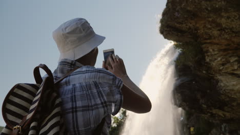 Eine-Frau-Steht-Unter-Einem-Wasserfall-Steinsdalsfossen-Macht-Ein-Foto-Darüber-Hängt-Ein-Felsen-Der-Majestätisch