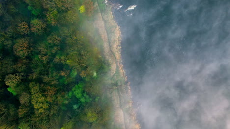 Top-down-aerial-shot-of-a-river-bank,-above-early-morning-fog-clouds