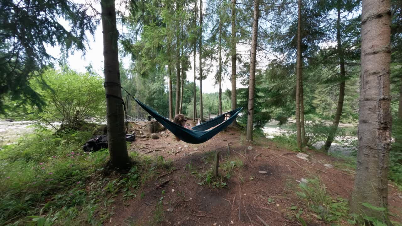 Relaxed woman in hammock holding mug of coffee in woodland nature