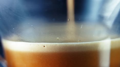 filling a clear glass with creamy brown coffee - macro shot