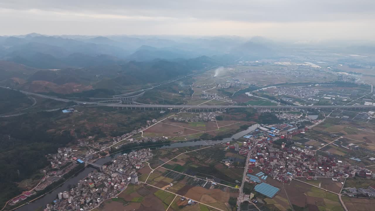 Aerial over Huishui County, Guizhou Province, China. Captures the contrast between a traditional river town, agricultural fields, and a massive modern highway infrastructure