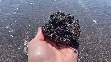 a handful of black sand in vichada black sand beach in santorini, greece