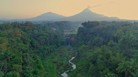 awatu purbo waterfall surrounded by lush forest with merapi volcano in the distance, aerial view