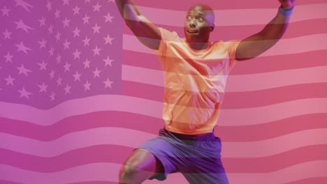 animation of flag of america over african american male basketball player jumping with ball