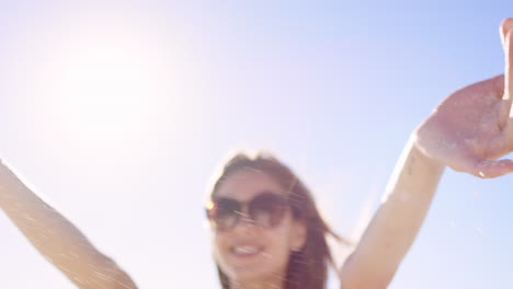 cerca de la mujer vertiendo arena corriendo a través de los dedos cámara lenta en la playa con llamarada solar y cielo azul