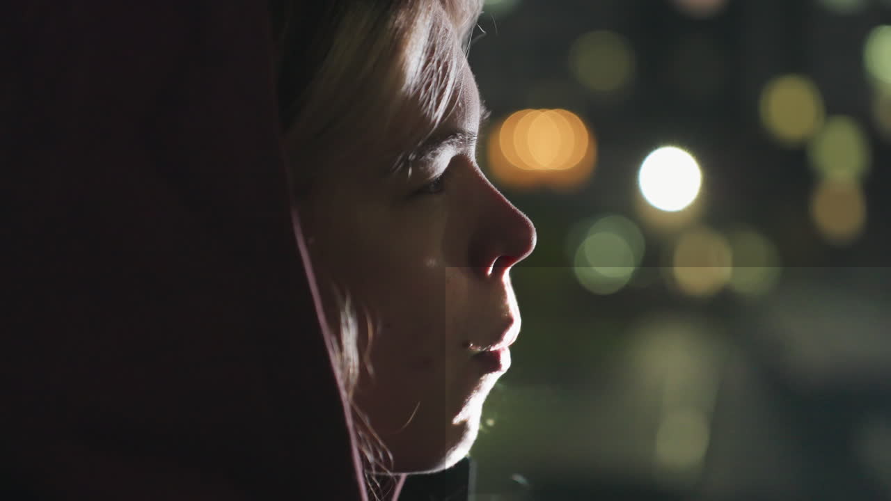 Close side profile captures hoodie wearing athlete enjoying dinner outdoors under urban night lights sipping water from plastic bottle while biting into fresh bread during twilight meal break