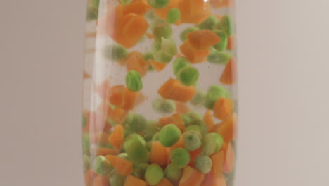 verduras mixtas guisantes verdes y zanahorias cayendo en agua filmado en 4k y crudo con estilo cinematográfico sobre un fondo blanco
