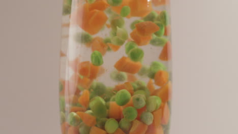 mixed vegetables green peas and carrots dropping in water shot on 4k and raw with cine style on a white background