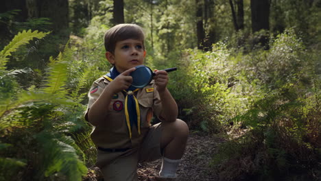 young boy scout exploring nature with magnifying glass