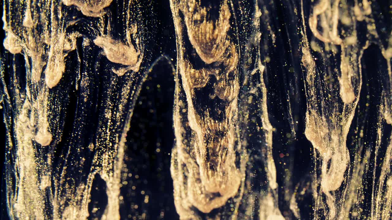 Golden ink particles flows in water as colorful chaos on the black background