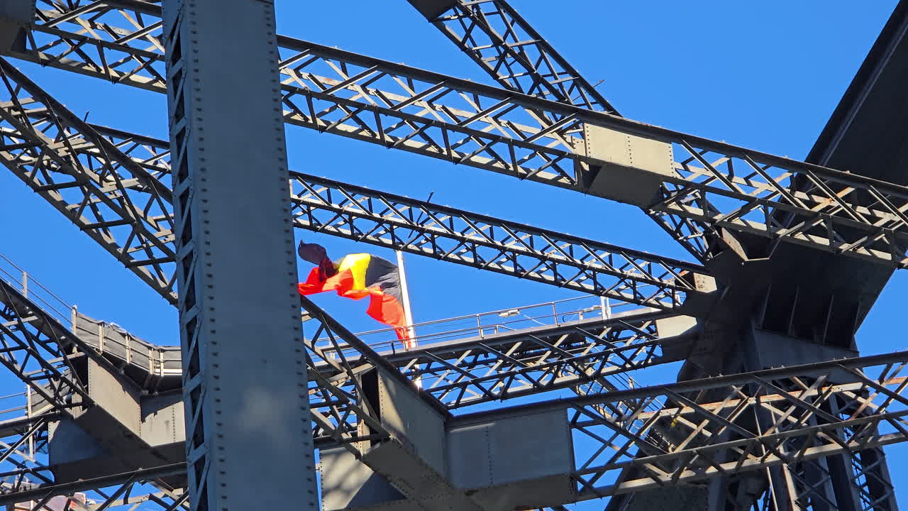 Sydney Harbour Bridge engineering framing the flying Aboriginal flag, representing Indigenous Australian heritage, culture, and national identity against bright blue sky