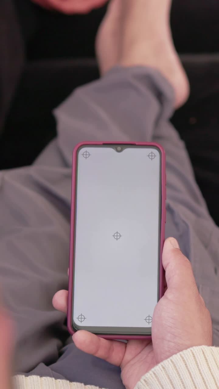 Video verticale: Telecamera che si sposta, mostra un ragazzo sul divano con maglietta color crema che inclina un telefono rosso per vedere uno schermo vuoto.