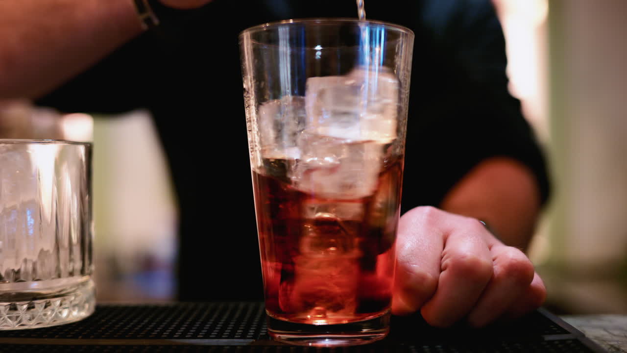 Primo piano di un barista che mescola un cocktail rosso con un cucchiaio da bar lungo in un bicchiere highball