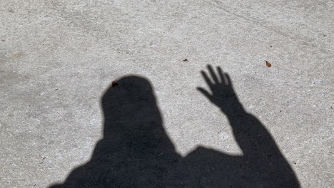 shadow of man waving hand that is open showing all fingers, standing on concrete