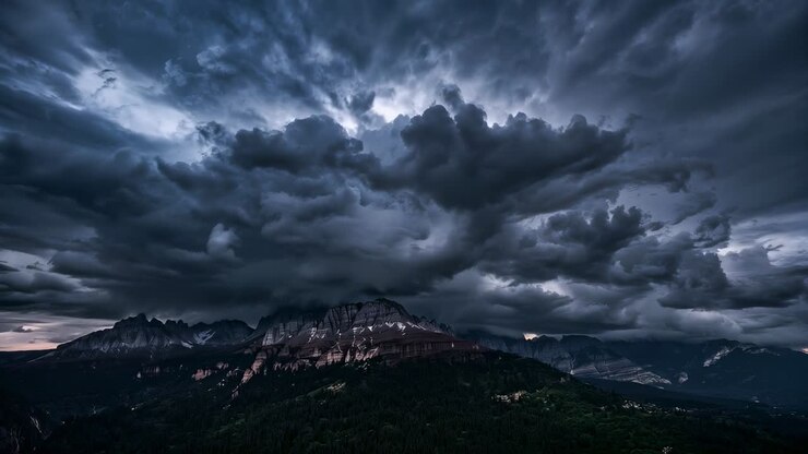 Massa compatta di nuvole temporalesche in rapido movimento che si addensa sopra la cresta della montagna al crepuscolo, con bagliore all'orizzonte