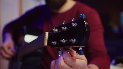 musical performer tuning his guitar by twisting the knobs