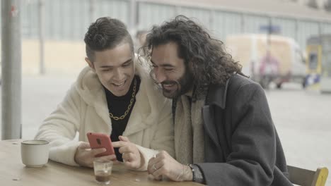 two friends looking at a smartphone in a cafe